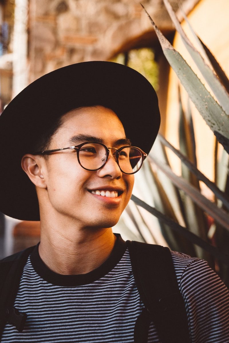 smiling man wearing black framed eyeglasses and hat